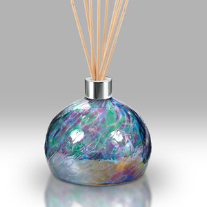 May include: A round glass diffuser bottle with a silver cap and wooden sticks. The bottle has a swirling iridescent pattern in shades of blue, green, and purple.