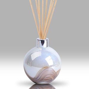 Op de afbeelding: Een witte en bruine glazen diffuserfles met een zilveren deksel en houten stokjes. De fles heeft een swirl-patroon.