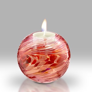 May include: A red glass candle holder with a white candle inside. The holder is round and has a swirling pattern.