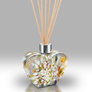 Könnte beinhalten: Eine herzförmige Glasdiffuserflasche mit silbernem Verschluss und Holzstäbchen. Die Flasche hat ein buntes Mosaikmuster in Weiß-, Gelb- und Brauntönen.