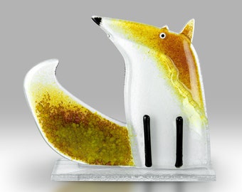May include: A glass sculpture of a fox standing on a clear glass base. The fox is white with yellow and brown accents. The fox's tail is curled up behind it.
