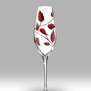 Könnte beinhalten: Eine klare Champagnerflöte aus Glas mit einem zarten Design aus roten Blättern und Ranken. Das Glas hat einen langen Stiel und eine breite Schale.