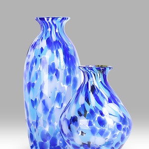 May include: Two blue and white glass vases with a speckled pattern. The larger vase is taller and narrower than the smaller vase.