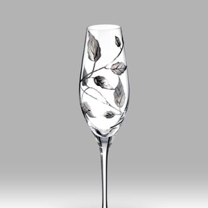 Op de afbeelding: Een heldere glazen champagnefluit met een zilveren bladontwerp. De bladeren zijn op het glas geschilderd en creëren een delicaat en elegant patroon.