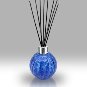 Può includere: Un diffusore in vetro blu con un colletto argentato e bastoncini neri. La bottiglia rotonda in vetro strutturato presenta un motivo marmorizzato. I bastoncini sono disposti a ventaglio, che si alzano dalla parte superiore della bottiglia. Il diffusore è progettato per la profumazione della casa.