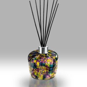 Może przedstawiać: Dekoracyjny szklany dyfuzor z kolorowym wzorem mozaiki w odcieniach żółtego, fioletowego i niebieskiego. Dyfuzor ma srebrny kołnierz i jest zwieńczony kilkoma czarnymi patyczkami.