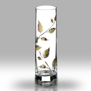 Op de afbeelding: Een heldere glazen vaas met een bladontwerp in goud. De vaas is cilindrisch en heeft een brede basis.