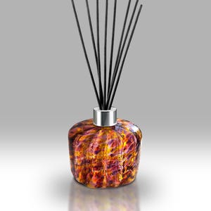 Può includere: Un diffusore a lamelle decorativo con un flacone in vetro strutturato nei toni dell'arancione, del giallo e del viola. Il flacone ha un colletto argentato ed è sormontato da lamelle nere, un elegante accessorio per la casa.