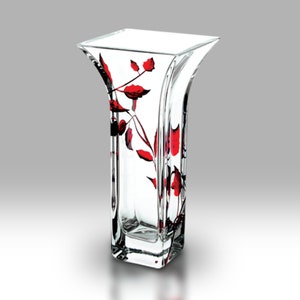 Peut inclure: Un vase en verre transparent avec une base carrée et une ouverture évasée. Le vase est décoré d'un motif floral rouge.
