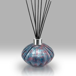 May include: A reed diffuser featuring a textured glass bottle in blue and red hues. The bottle has a silver collar and is filled with black diffuser sticks. A decorative home fragrance accessory.