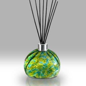 May include: A decorative glass diffuser with a round, bulbous shape. The glass is a mix of green and blue hues. Black reeds extend upwards from a silver-coloured collar. The diffuser is designed for home fragrance.