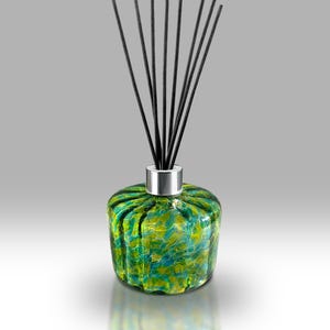 May include: A decorative glass diffuser bottle with a green and yellow mottled pattern. The bottle has a silver collar and is topped with several black diffuser sticks. The bottle is round and has a textured surface.