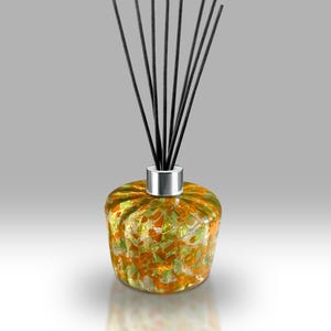 May include: A decorative glass diffuser with black reeds. The round, textured glass vessel features a blend of orange and green colors. A silver collar secures the reeds, which fan out from the top.