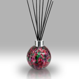 May include: A decorative glass diffuser with a round, speckled design in shades of red, green, and purple. The diffuser has a silver collar and is filled with black reeds, a stylish home fragrance accessory.