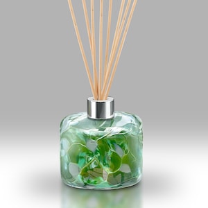 May include: A green glass diffuser bottle with a silver cap and wooden sticks. The bottle has a textured, rippled surface.