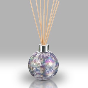 May include: A round glass diffuser bottle with a silver lid and a floral pattern. The bottle is filled with a clear liquid and has wooden sticks sticking out of the top.