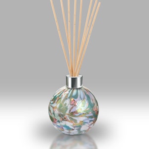 May include: A round glass diffuser bottle with a silver cap and wooden sticks. The bottle has a colorful, iridescent design with shades of green, white, and gold.