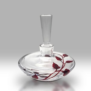 May include: A clear glass bottle with a red floral design. The bottle has a round base and a long, thin neck.