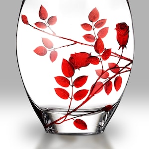 May include: A clear glass vase with a red rose and leaves design. The vase is oval shaped and has a wide mouth.