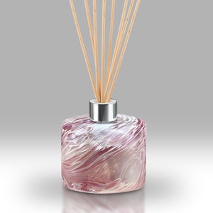 Könnte beinhalten: Eine Diffusionsflasche aus Glas mit rosa und weißen Wirbeln, einem silbernen Verschluss und Holzstäbchen.
