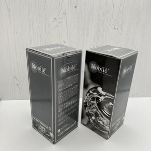 May include: Two black boxes with the text "Nobil&eacute; Glass & Culture" and "The Home of Handmade Glass" on them. The boxes are on a white wooden surface.