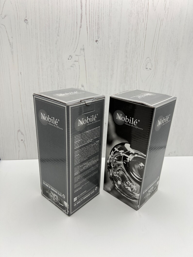 May include: Two black boxes with the text "Nobil&eacute; Glass & Culture" and "The Home of Handmade Glass" on them. The boxes are on a white wooden surface.