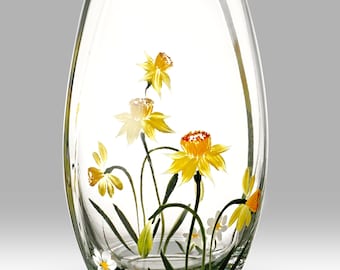 May include: A clear glass vase with a painted floral design. The vase features yellow daffodils and white daisies with green stems and leaves. The vase has an oval shape and is suitable for displaying flowers.