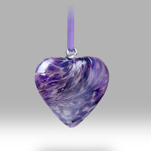 May include: A purple glass heart ornament with a swirl pattern, hanging from a purple ribbon.