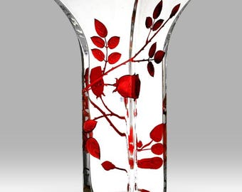 May include: A clear glass vase with a square base and flared top. The vase is decorated with a red rose and leaf design. The floral pattern is painted on the exterior of the vase, creating a striking contrast against the clear glass.