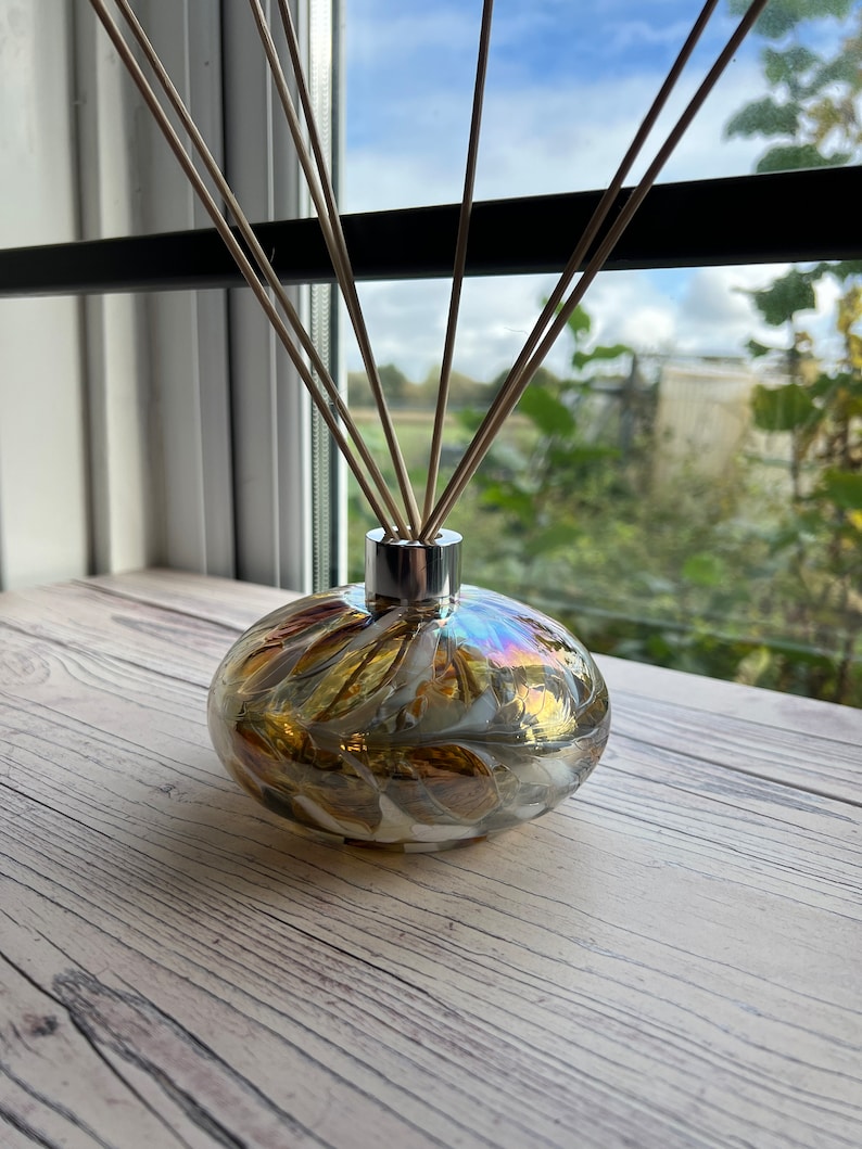 May include: A diffuser bottle with a swirl pattern in shades of gold, white, and brown. The bottle has a silver cap and is filled with reeds.