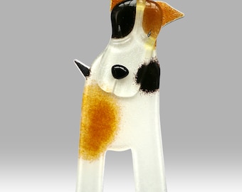 May include: A glass figurine of a white, brown, and black dog with a spotted pattern. The dog is standing on a clear glass base.