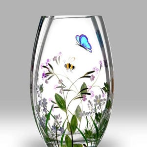 Può includere: Un vaso di vetro trasparente con un disegno dipinto a mano di fiori selvatici, un'ape e una farfalla. Il vaso ha una forma ovale arrotondata e un'ampia apertura.