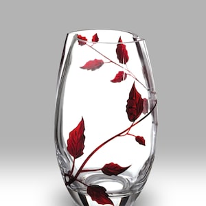 Könnte beinhalten: Eine klare Glasvase mit rotem Blumendesign. Die Vase hat eine abgerundete, ovale Form und ein zartes Stieldesign.