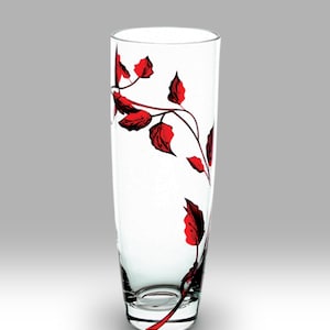 Op de afbeelding: Een heldere glazen vaas met een rood bloemenontwerp. De vaas is hoog en slank met een ronde bodem.
