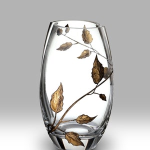 May include: Clear glass vase with an oval shape and a decorative gold leaf design. The leaves and stems are painted on the exterior of the vase. The vase has a smooth, polished finish and is suitable for displaying flowers or as a decorative accent.