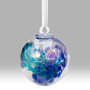 Puede incluir: Una bola de cristal transparente con un dise&ntilde;o abstracto en tonos azules, turquesas y morados. Est&aacute; suspendida por una cinta blanca. El dise&ntilde;o parece arremolinado y en capas.