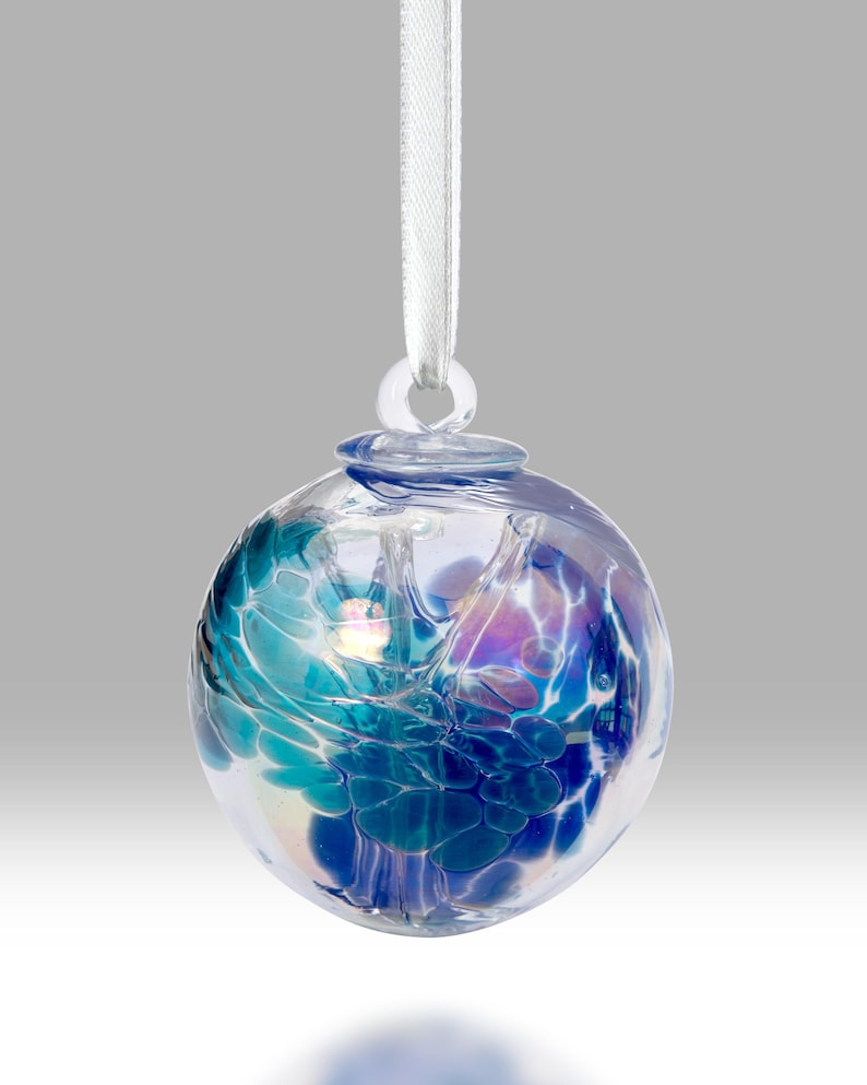 Puede incluir: Una bola de cristal transparente con un dise&ntilde;o abstracto en tonos azules, turquesas y morados. Est&aacute; suspendida por una cinta blanca. El dise&ntilde;o parece arremolinado y en capas.