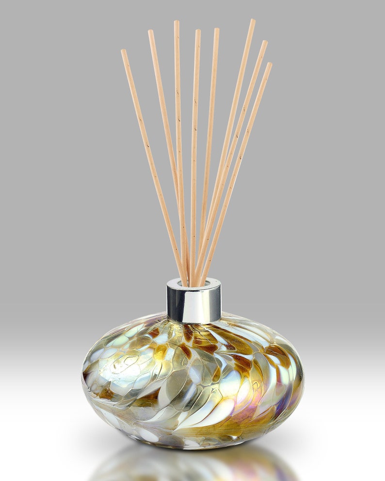 May include: A glass diffuser bottle with a silver cap and a swirl pattern in shades of brown, gold, and white. The bottle is filled with a clear liquid and has wooden sticks sticking out of the top.