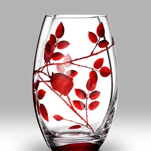 May include: A clear glass vase with a red rose and leaves design. The vase has a rounded bottom and a wide opening.
