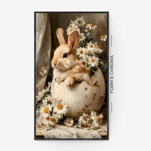 Op de afbeelding: Een ingelijste print met een lichtbruin konijn dat uit een gebarsten ei komt, omringd door witte en gele bloemen. Het kunstwerk heeft een vintage esthetiek, met zachte belichting en een neutraal kleurenpalet. De tekst "FORM & CHROMA" is zichtbaar.