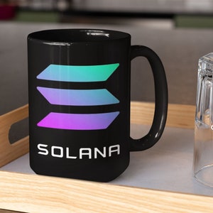May include: A black ceramic mug with a white handle. The mug has a colorful graphic of three stacked bars and the word "SOLANA" printed in white below the graphic.