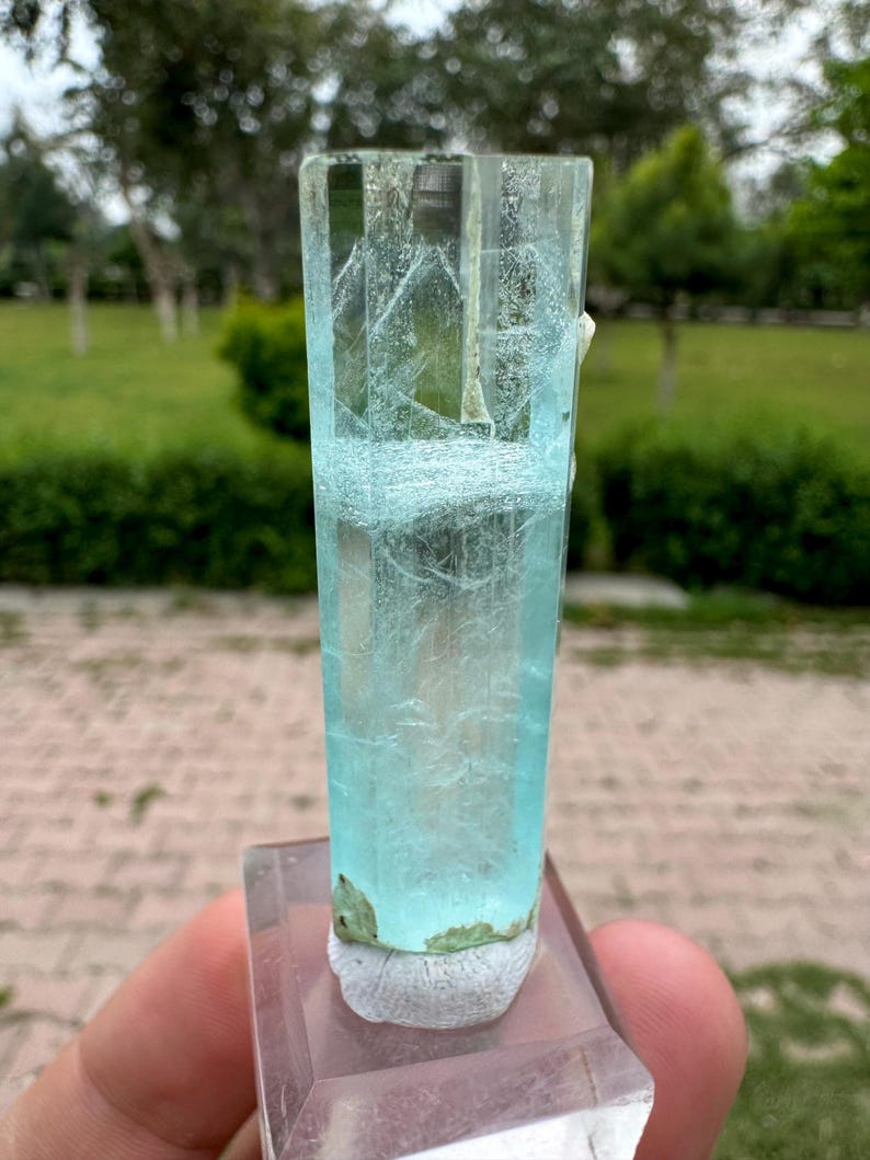 Pu&ograve; includere: Cristallo di acquamarina trasparente e rettangolare con una tonalit&agrave; azzurra. Il cristallo &egrave; montato su una base trasparente e rettangolare. Il cristallo presenta strutture interne visibili ed &egrave; sostenuto da un materiale bianco strutturato.