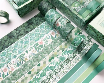 May include: A collection of green washi tapes with various botanical patterns, including leaves and floral designs. The tapes are displayed in decorative boxes and rolls, showcasing a range of shades from light to dark green.