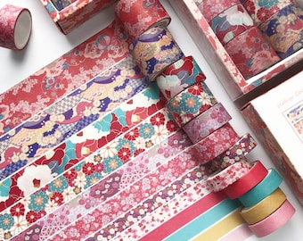 May include: A set of 12 washi tapes with floral and geometric patterns in shades of red, pink, blue, and green. The tapes are arranged in a fan shape on a white surface.