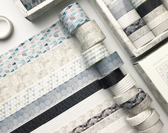 May include: A collection of washi tapes with geometric patterns in shades of gray, white, and blue. The tapes are arranged in rows, with the ends of each tape visible. The tapes are in a variety of patterns, including triangles, hexagons, and lines.