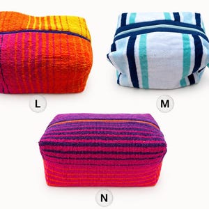 May include: Three rectangular zippered pouches made of textured terry cloth fabric. Pouch L features orange, yellow, and pink stripes. Pouch M has blue, white, and teal stripes with a side handle. Pouch N displays purple, pink, and orange stripes.