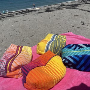 May include: Four rectangular zippered pouches made of textured fabric. One pouch features a yellow and blue leaf pattern, another has a blue and teal striped design, and two pouches display vibrant orange, red, and purple wavy line patterns.