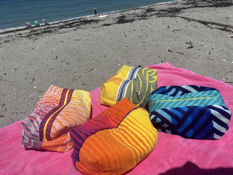 May include: Four rectangular zippered pouches made of textured fabric. One pouch features a yellow and blue leaf pattern, another has a blue and teal striped design, and two pouches display vibrant orange, red, and purple wavy line patterns.