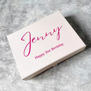 May include: A white gift box with a pink inscription that reads "Jenny Happy 21st Birthday".
