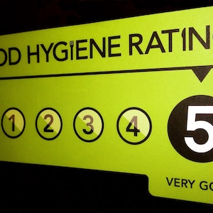 以下が含まれることがあります： 明るい緑色の食品衛生評価サイン。上部に「FOOD HYGIENE RATING」の文字。下には0から5までの数字が入った円があり、5は大きな黒い円で囲まれ、その下に「VERY GOOD」の文字があります。